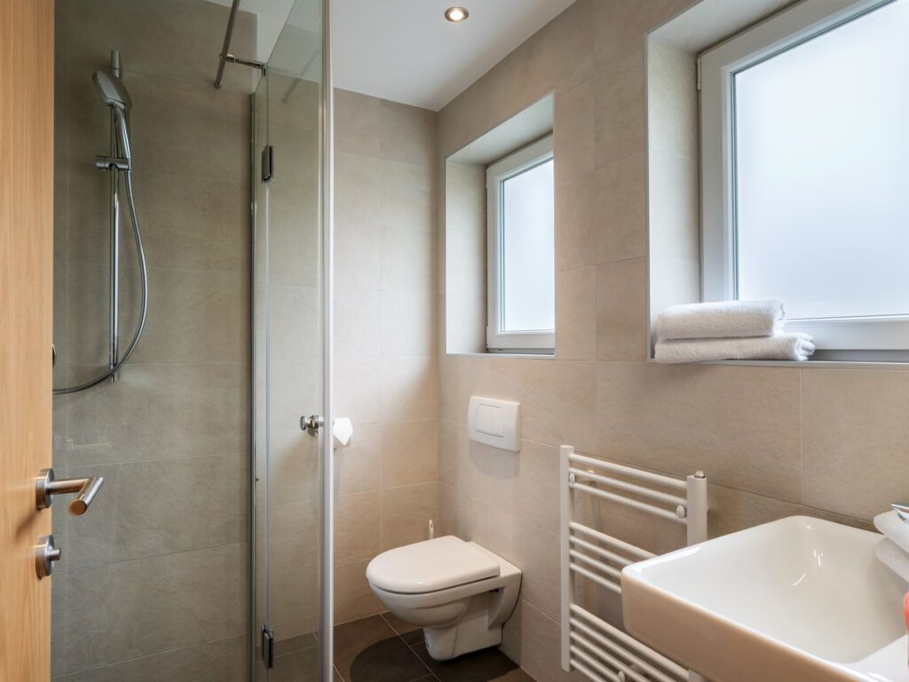 Moderne Badezimmereinrichtung mit Glasduschkabine, Toilette, Handtuchhalter und natürlichem Licht, das durch ein Milchglasfenster fällt.