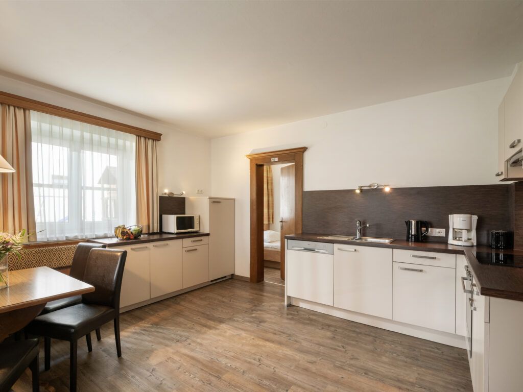 Eine gut beleuchtete, moderne Küche mit Holzboden, weißen Schränken und Geräten aus Edelstahl.
