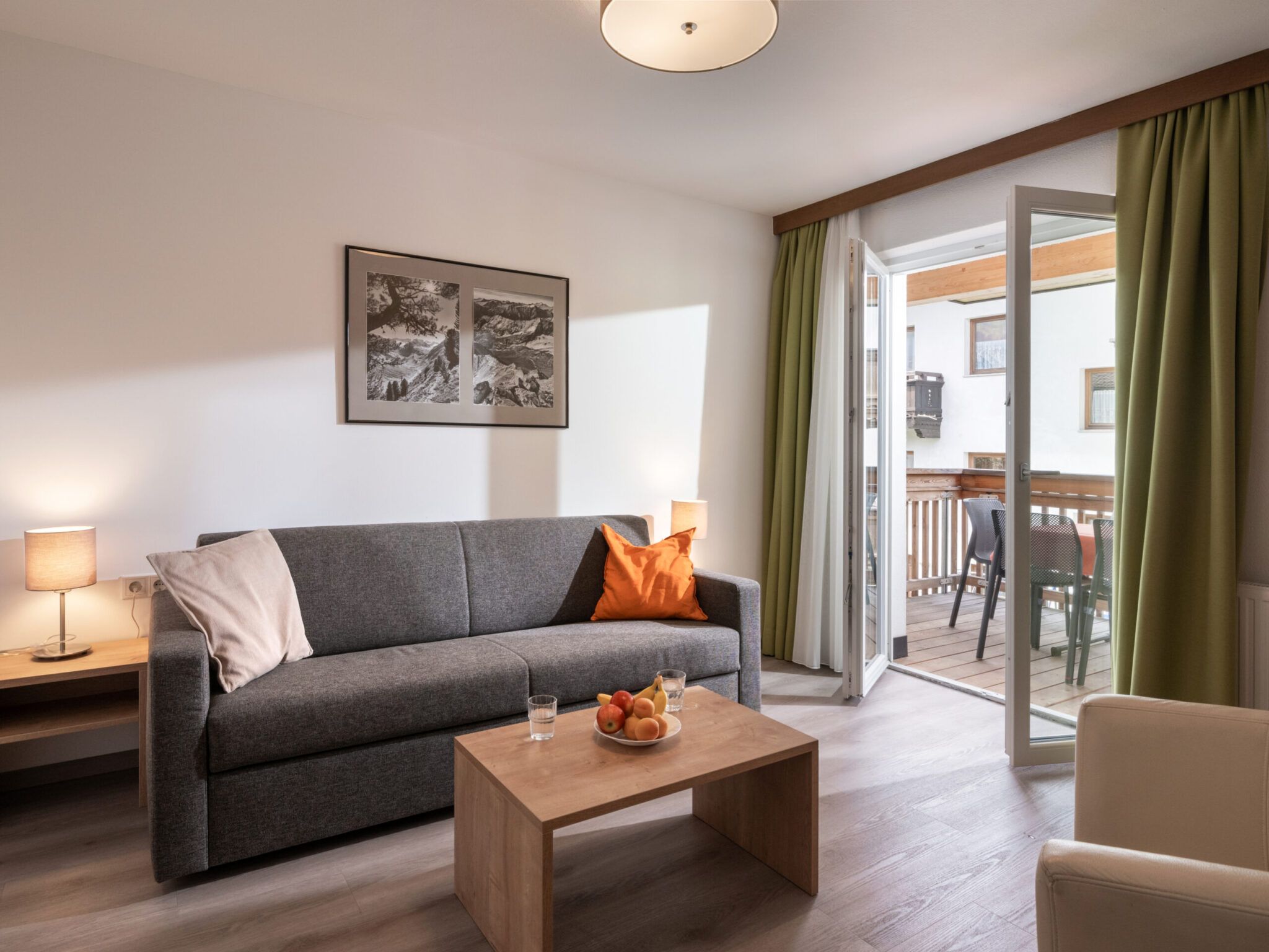 Ein gemütliches, gut beleuchtetes Wohnzimmer mit einem modernen Sofa, einem Couchtisch aus Holz und einer offenen Balkontür.