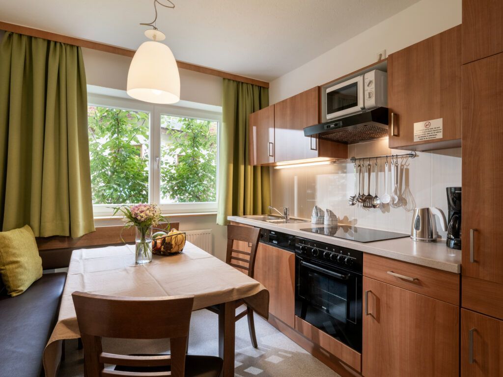 Moderne Kücheneinrichtung mit Holzschränken, Geräten aus Edelstahl und einem Essbereich mit Blick auf ein Fenster.