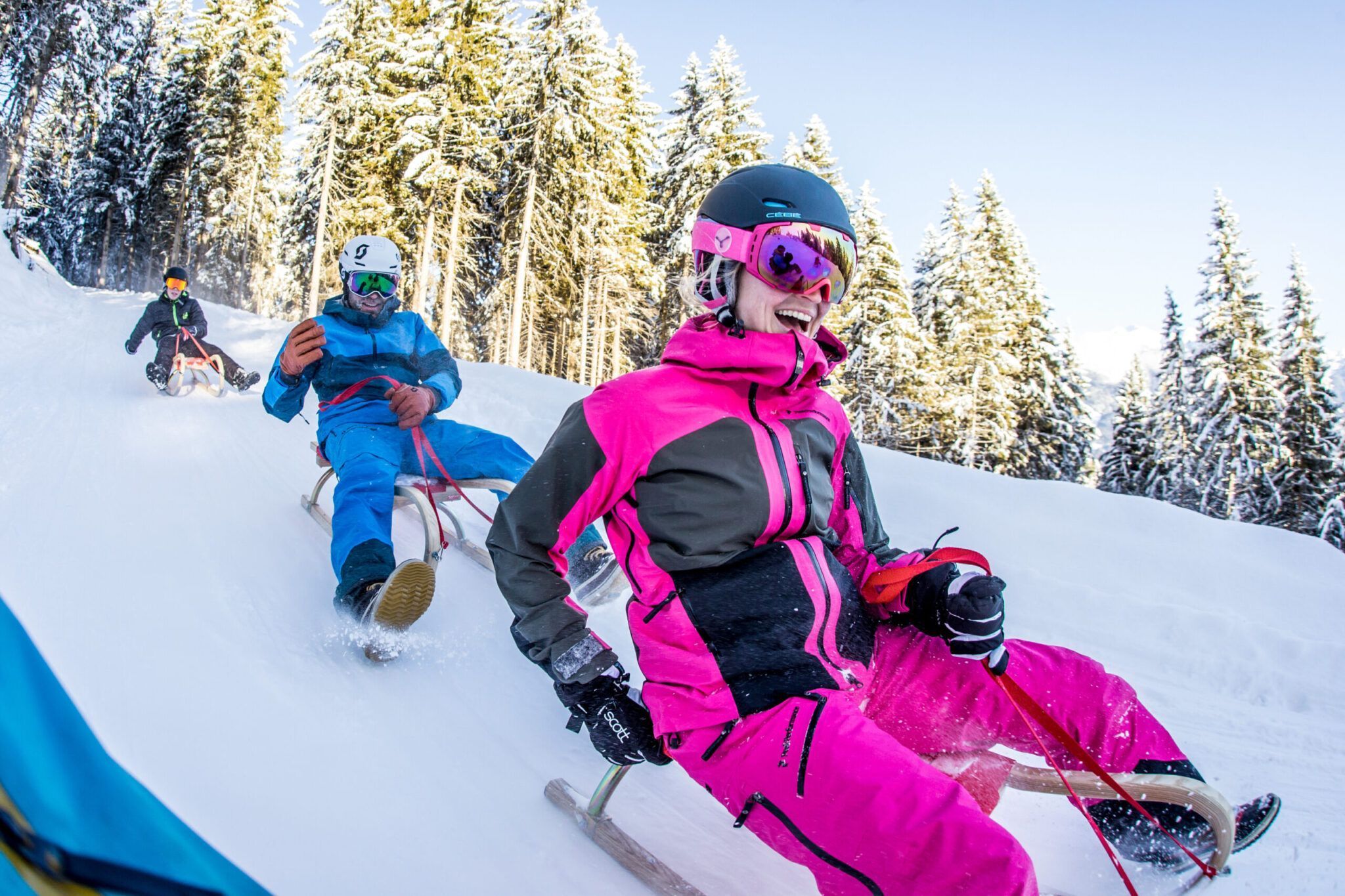 Eine Gruppe von Menschen in Winterkleidung rodelt einen schneebedeckten Hang hinunter, umgeben von schneebedeckten Bäumen. Eine Gruppe von Menschen in Winterkleidung rodelt einen schneebedeckten Hang hinunter, umgeben von schneebedeckten Bäumen.