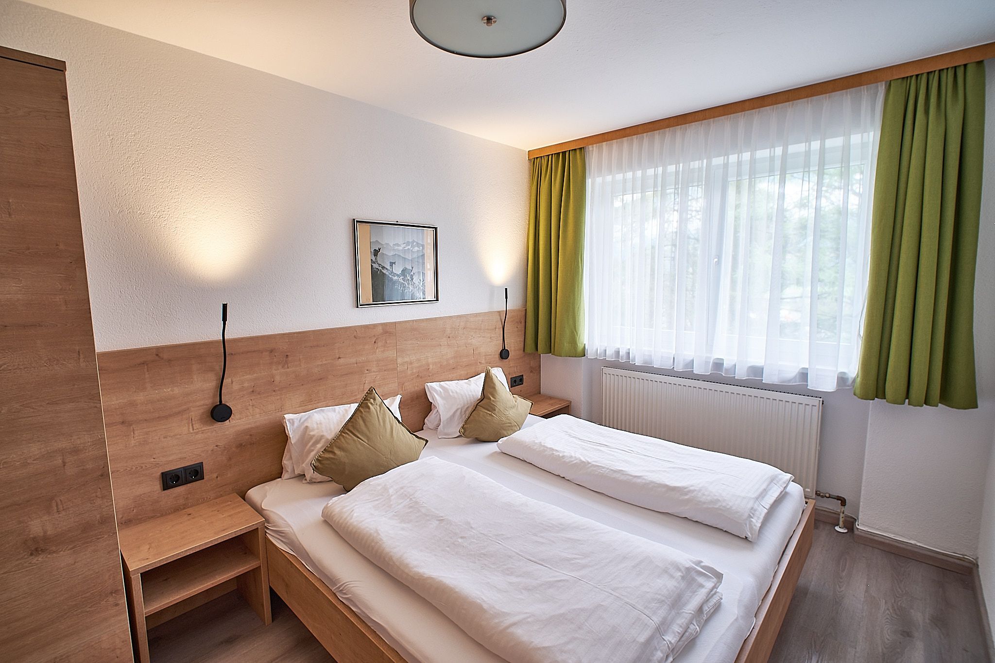 Een gezellige hotelkamer met een tweepersoonsbed, houten hoofdeinde, groene gordijnen en wandlampen.