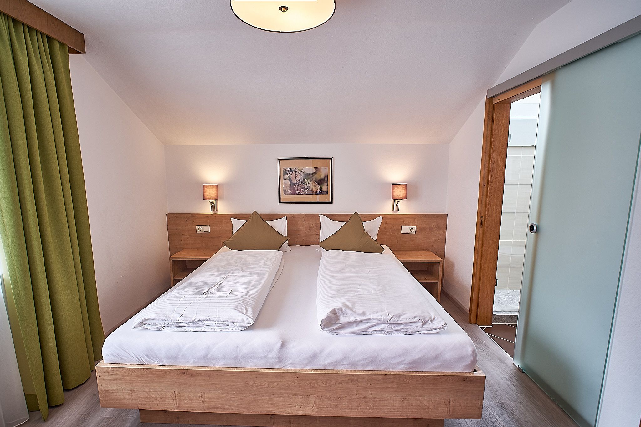 Gemütliches Schlafzimmer mit einem Doppelbett, grünen Vorhängen und einem Gemälde über dem Kopfteil.
